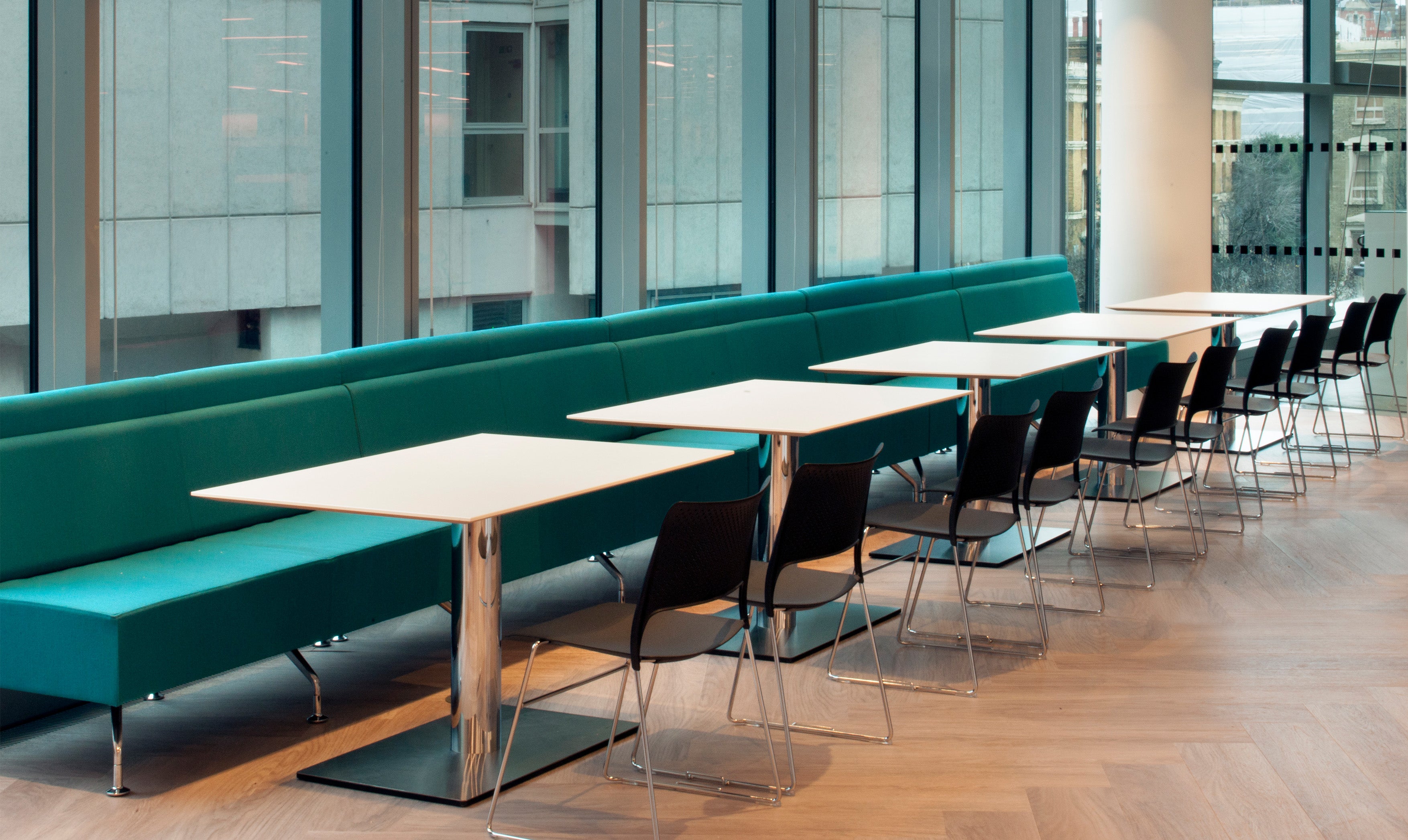 Modern office break room with teal benches and white tables.